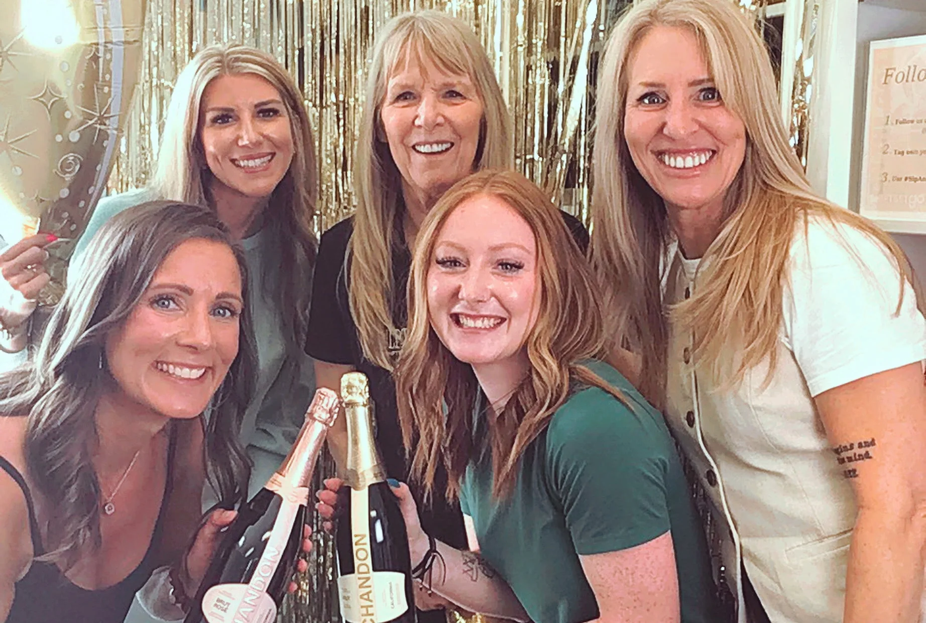 Guests raising bottles of bubbly together in front of the gold fringe backdrop