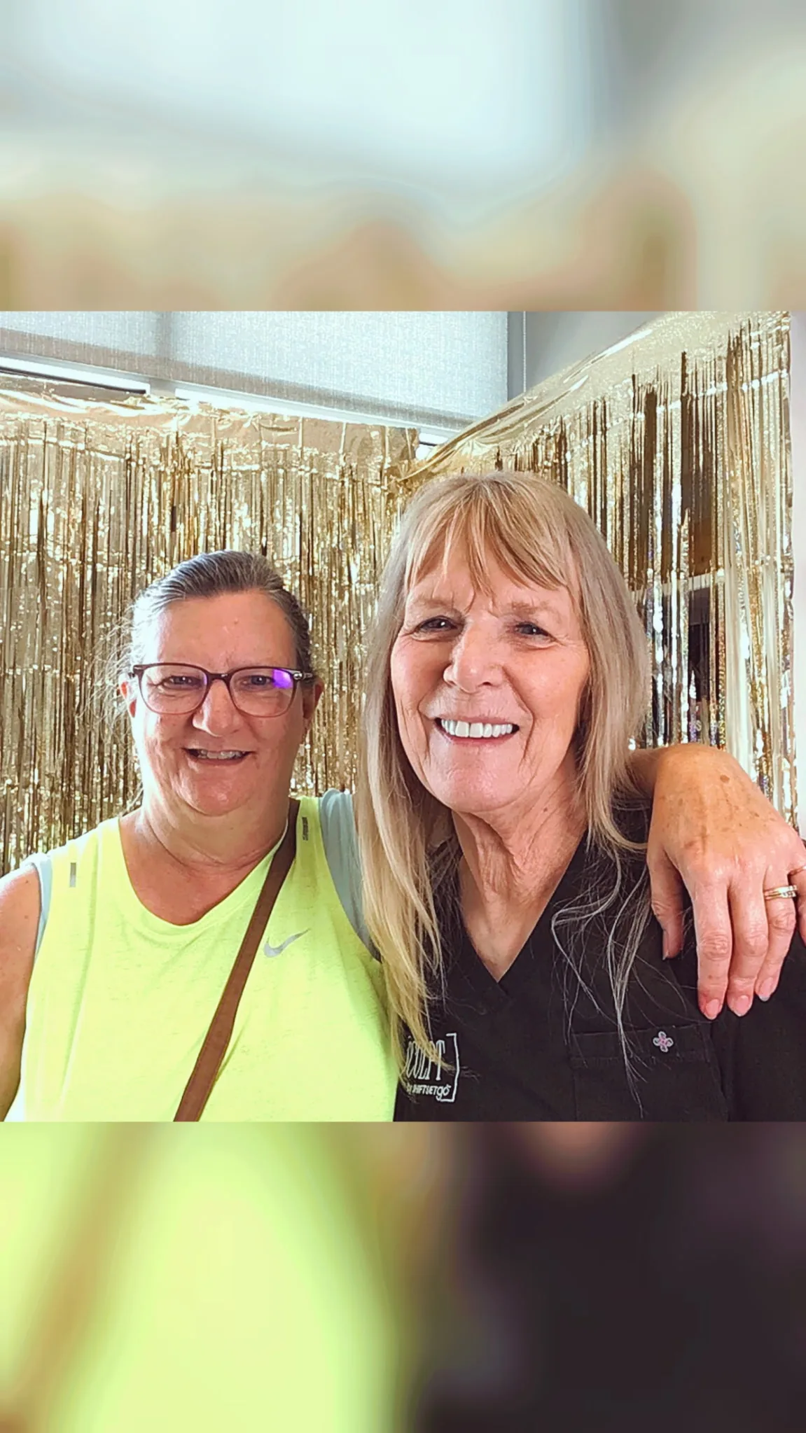Two friends smiling in front of the gold fringe backdrop